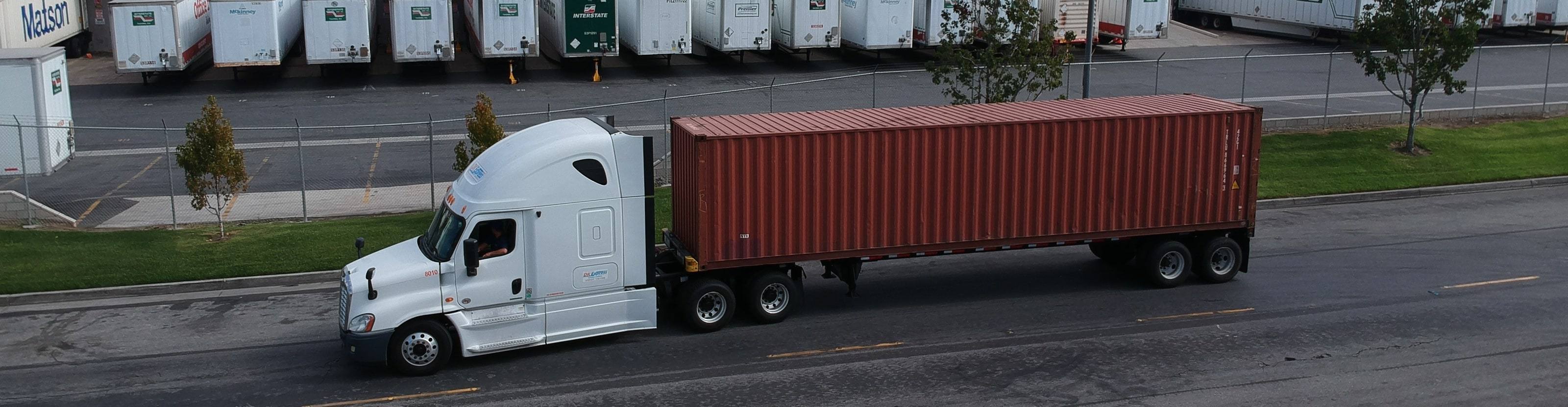 DK Express tractor hauling a container along a road next to a trailer yard