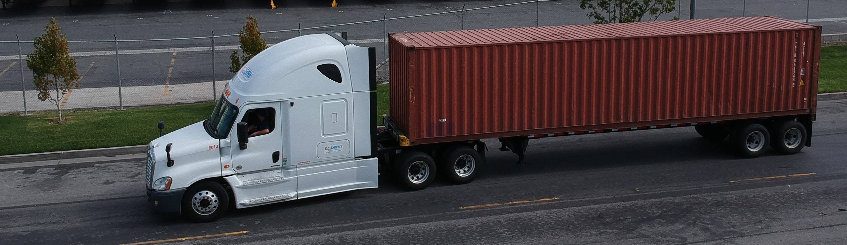 DK Express tractor hauling a container past a trailer yard